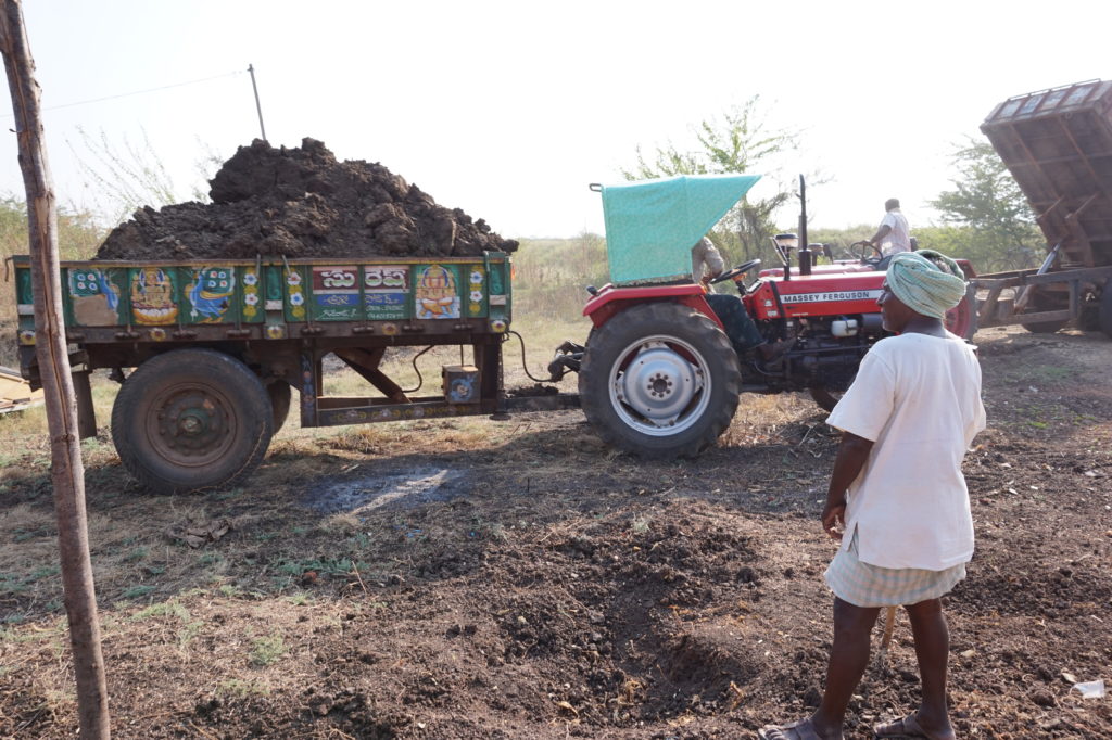 A tractor delivers a load of dirt to the land for the construction of the Good News Visions Prayer Hall, with Yesupadem looking on.